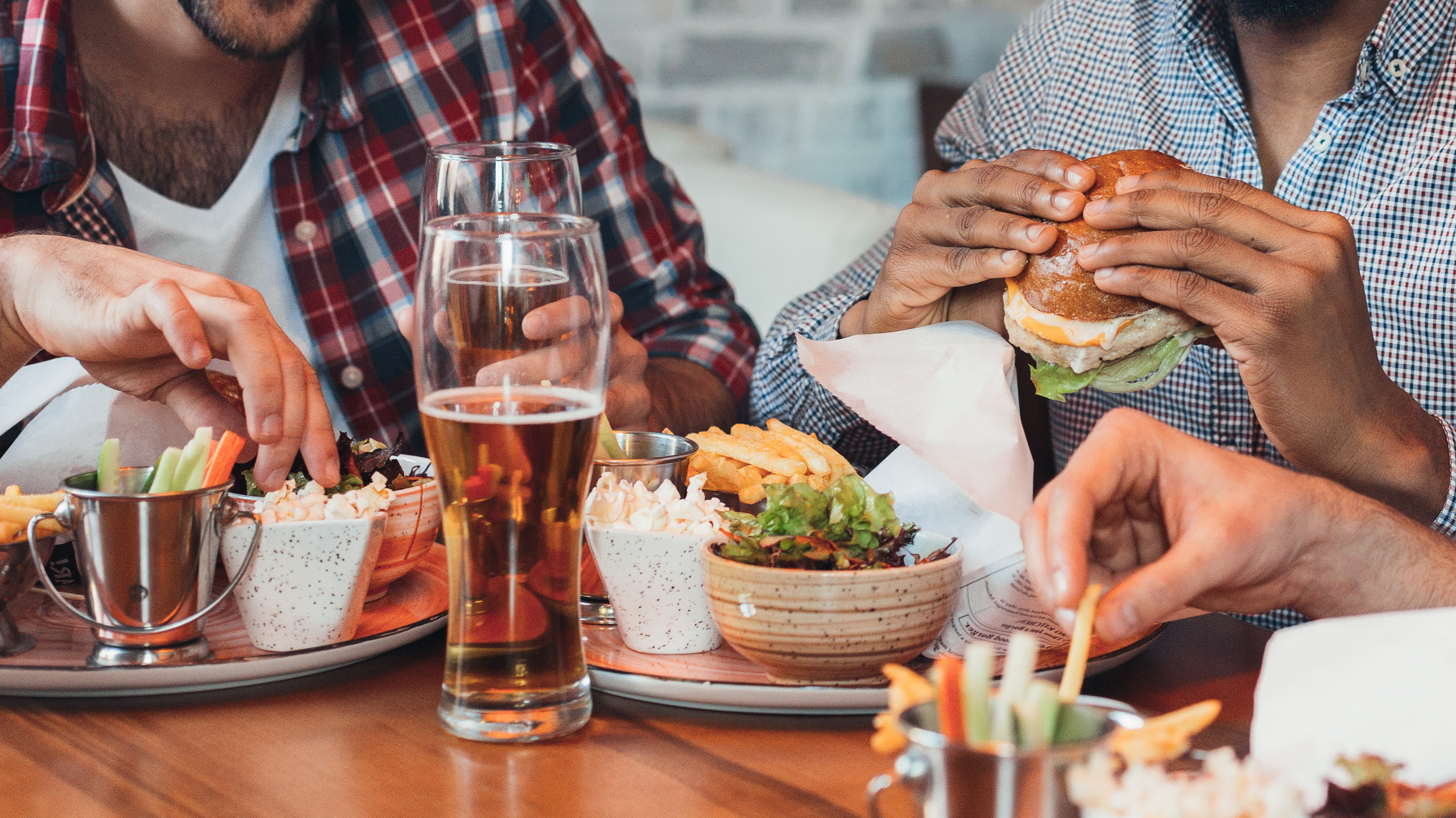 three-men-enjoying-burgers-and-beer-in-bar-ABXF58S